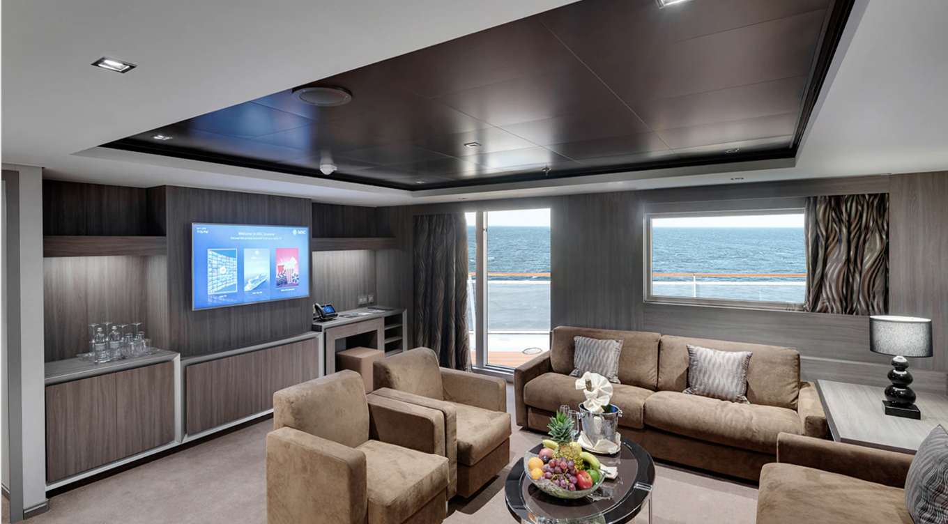 Step into the luxurious Royal Suite on Seascape within the Yacht Club, featuring an inviting living room adorned with green couches and a TV, offering an exclusive and opulent experience. 
